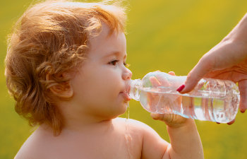 baby boy with curly blond hair drinking water